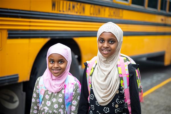two girls smiling with a bus in the background